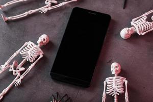 Four skeletons are lying near the smartphone on a dark background. photo