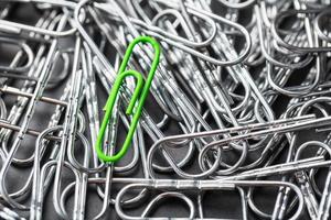 The green paper clip stands out against a textured background of silver paper clips photo