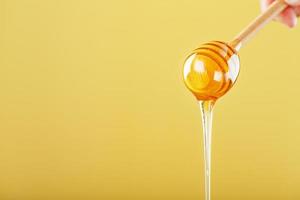 Honey drips in a thin stream from a honey dipper on a yellow background. photo