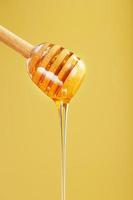 la miel natural fluye desde un balde de miel sobre un fondo amarillo. foto