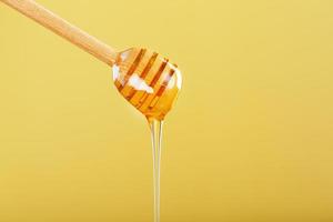 Golden honey trickles from a wooden honey dipper on a yellow background photo