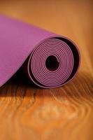 A lilac-colored yoga mat is spread out in a roll on the wooden floor. photo