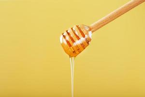 Honey drips in a thin stream from a honey dipper on a yellow background. photo