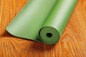 A green yoga mat is laid out in a roll on the wooden floor. photo