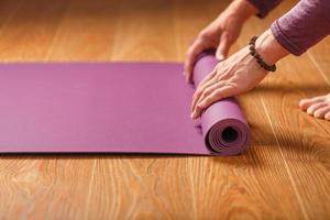 A girl lays out a lilac yoga mat before a workout practice at home on a wooden floor. photo