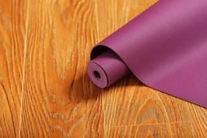 A lilac-colored yoga mat is spread out in a roll on the wooden floor. photo