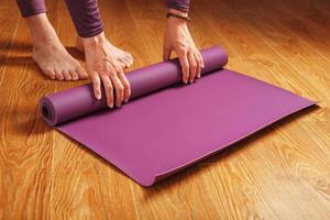 una niña dobla una alfombra de yoga lila después de un entrenamiento de práctica en un piso de madera foto