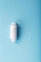 A spool of white thread with a needle on a blue background. photo