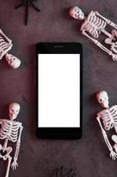Four skeletons are lying near the smartphone on a dark background. photo