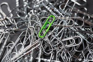 The green paper clip stands out against a textured background of silver paper clips photo