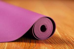 An unfolded lilac-colored yoga mat is unfolded on the wooden floor. photo