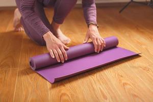 A man lays out a lilac yoga mat on the wooden floor of a house photo