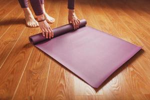 las manos de una mujer colocan una alfombra de yoga o fitness lila antes de una práctica de entrenamiento en casa en un suelo de madera. foto