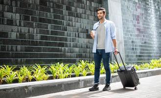 Young caucasian man drinking coffee and pulling the suitcase waiting his friend for travel together. photo