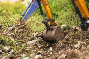 Backhoe digging soil at construction site. Bucket of backhoe digging soil. Clearing and grubbing. Digger working at road construction site. Earth moving machine. Excavation vehicle. Land development. photo