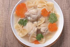 Macaroni soup with chicken thighs in clear broth with carrots.on an rustic old wood background. photo