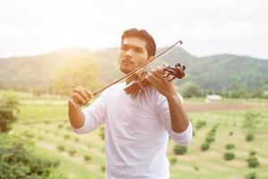 joven músico hipster tocando el violín en el estilo de vida al aire libre de la naturaleza detrás de la montaña. foto