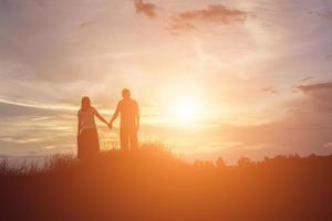 a silhouette of a man and woman holding hands with each other, walking together. photo