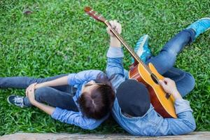 hombre hipster tocando la guitarra para su novia al aire libre contra la pared de ladrillo, disfrutando juntos. foto