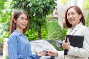 Beautiful young woman holding car keys and handing to Asian female customer. photo