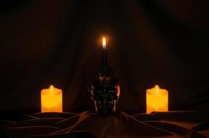 fondo de halloween aterrador con vela en el cráneo se pone en tela negra con velas de enfoque borroso en la parte posterior. foto