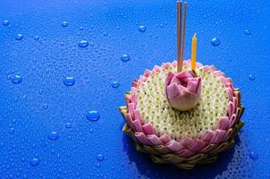 Pink lotus petal krathong for Thailand Loy Krathong festival decorates with its flower, crown flower, incense stick and candle on blue background with water drop. photo