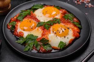 Shakshuka, a dish with fried eggs with tomato sauce, sweet pepper, garlic, onions, spices and herbs photo