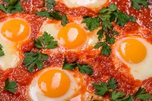 Shakshuka, a dish with fried eggs with tomato sauce, sweet pepper, garlic, onions, spices and herbs photo