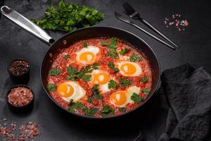Shakshuka, a dish with fried eggs with tomato sauce, sweet pepper, garlic, onions, spices and herbs photo