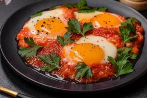 Shakshuka, a dish with fried eggs with tomato sauce, sweet pepper, garlic, onions, spices and herbs photo