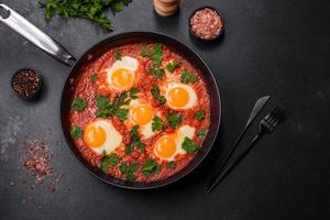 Shakshuka, a dish with fried eggs with tomato sauce, sweet pepper, garlic, onions, spices and herbs photo