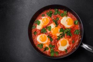 Shakshuka, a dish with fried eggs with tomato sauce, sweet pepper, garlic, onions, spices and herbs photo