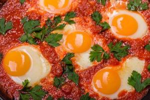 Shakshuka, a dish with fried eggs with tomato sauce, sweet pepper, garlic, onions, spices and herbs photo