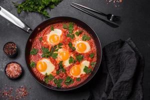 Shakshuka, a dish with fried eggs with tomato sauce, sweet pepper, garlic, onions, spices and herbs photo