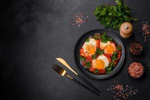 Shakshuka, a dish with fried eggs with tomato sauce, sweet pepper, garlic, onions, spices and herbs photo