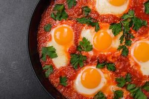 Shakshuka, a dish with fried eggs with tomato sauce, sweet pepper, garlic, onions, spices and herbs photo