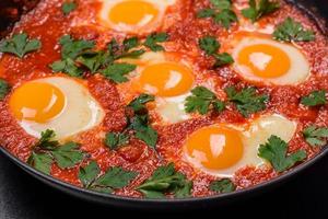 Shakshuka, a dish with fried eggs with tomato sauce, sweet pepper, garlic, onions, spices and herbs photo