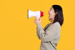 Beautiful Asian woman holding a megaphone and shouting out on a yellow background. She was excited in the side view. photo