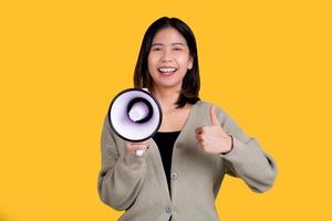 Excited Asian woman screaming at megaphone and thumbs up isolated on yellow background studio portrait. photo