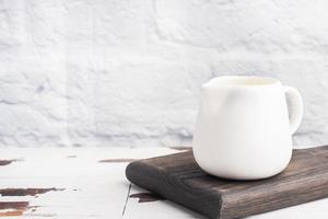 White ceramic milk jug with fresh milk on a gray background. Copy space. photo