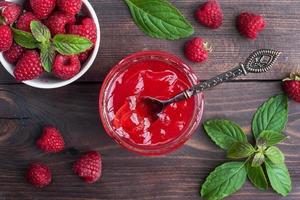 Homemade raspberry jam in a glass jar and fresh raspberries with mint on a wooden rustic background. Copy space photo