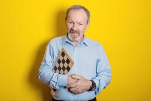 smiling elderly man holding checkers and chess board in his hands on yellow background photo