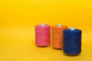 Three multi-colored large spools of thread stand one after another on a yellow background. Side view. photo