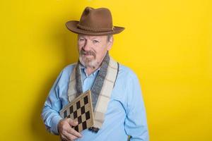 cute handsome senior man with hat and scarf holding a chessboard in his hands photo