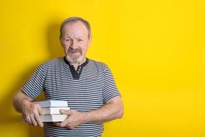 cute senior men holding a stack of books on yellow background. copy space photo