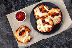 Mini pizza as mummy for kids with cheese, olives and ketchup. Funny crazy Halloween food for children. photo