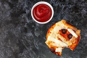 mini pizza como momia para niños con queso, aceitunas y ketchup. divertida comida loca de halloween para niños.