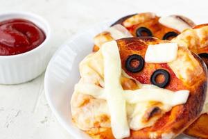 Mini pizza as mummy for kids with cheese, olives and ketchup. Funny crazy Halloween food for children photo