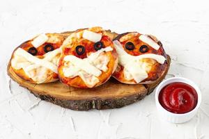 mini pizza como momia para niños con queso, aceitunas y ketchup. divertida comida loca de halloween para niños foto