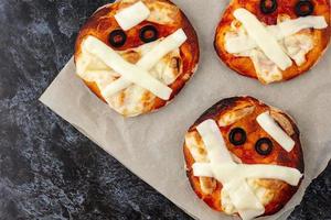 Mini pizza as mummy for kids with cheese, olives and ketchup. Funny crazy Halloween food for children. photo